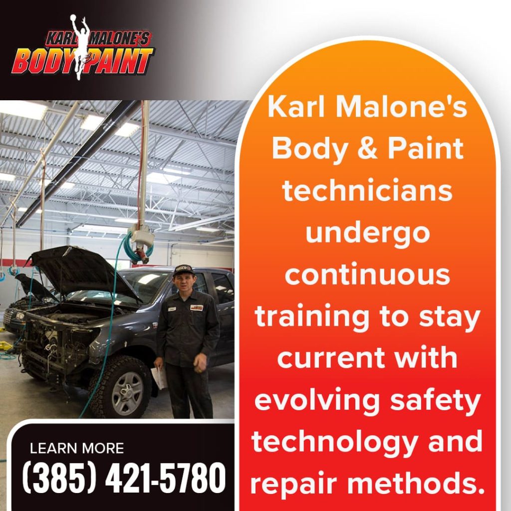 Karl Malone's Body & Paint technician standing in front of two damaged cars in a modern auto body shop, showcasing ongoing training in collision repair.